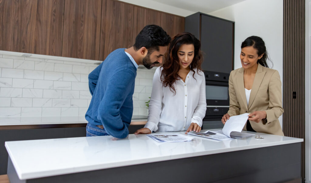 Happy real estate agent showing brochures to an Indian couple at an open house - commercial activity concepts